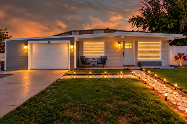 Single-story exterior with a flat roofline, white brick and gray siding, a stone pathway, and a well-maintained lawn