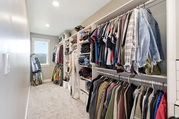Built-in closet system with multiple shelving tiers and hanging rods, recessed ceiling lighting, a single window, and light-colored carpeting