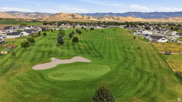 Expansive green space featuring a golf course, sand trap, putting green, and scattered evergreen trees, bordered by residential properties