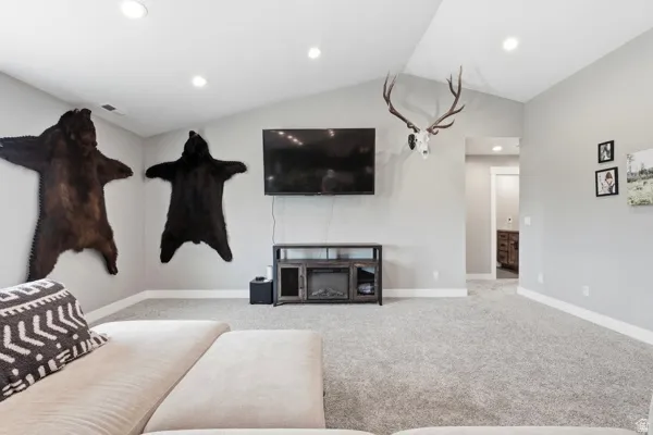 Vaulted ceiling, recessed lighting, wall-to-wall carpeting, wood-finish media console, and an electric fireplace insert