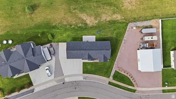 Expansive gravel lot with a large white outbuilding, concrete driveway, and abundant green space
