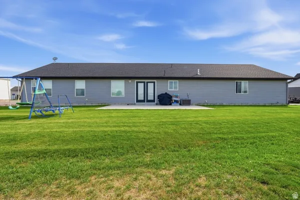 Expansive rear yard featuring a large concrete patio, double glass panel doors, multiple windows, and horizontal siding