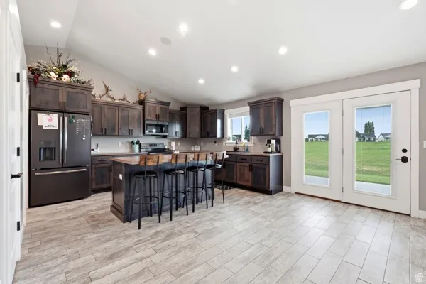 Kitchen featuring dark wood cabinetry, a large kitchen island, wood-finish countertops, black appliances, and light-toned tile flooring