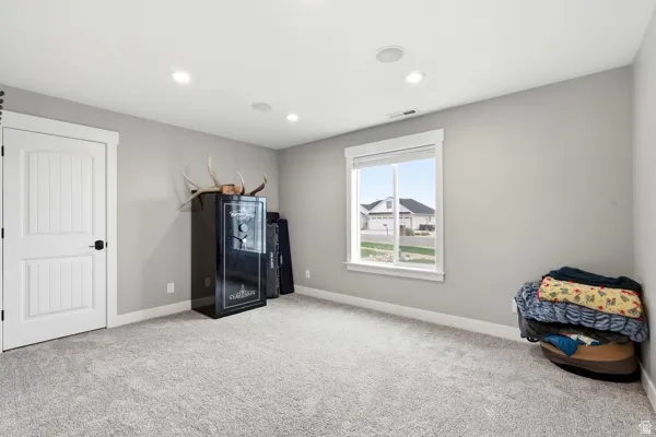 Recessed lighting, light gray carpet, window with white trim, solid paneled door with black hardware, and light gray walls
