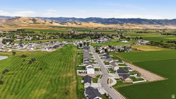 Residential development featuring paved streets and established homes, bordered by expansive green fields and distant mountain ranges