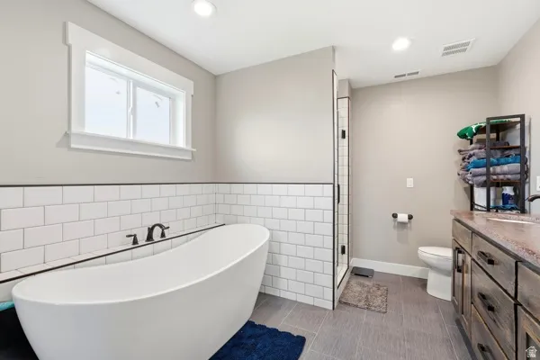 Freestanding soaking tub, white subway tile surround, dark wood-finish vanity with countertop, glass-enclosed shower, and tiled flooring