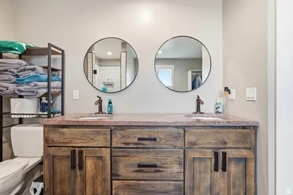 Dual round mirrors above a wood-finish vanity with dual sinks, bronze-finish fixtures, and a stone-finish countertop