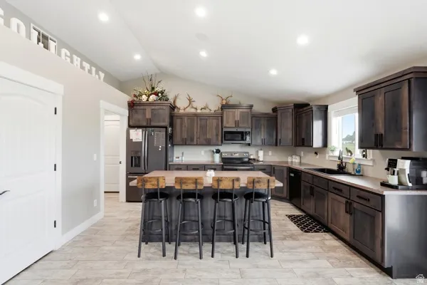Kitchen featuring vaulted ceilings, recessed lighting, wood-finish cabinetry, a central island with seating, and light-toned tile flooring