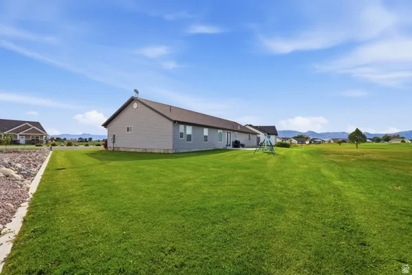 Expansive lawn area with a single-story residence featuring light gray siding and a dark roof