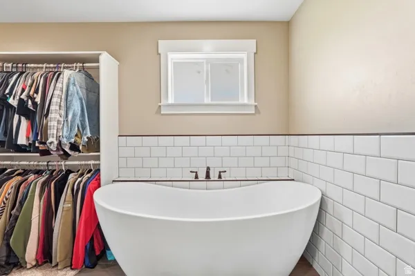 Freestanding soaking tub with dark bronze fixtures, white subway tile surround, built-in open shelving, and a framed window