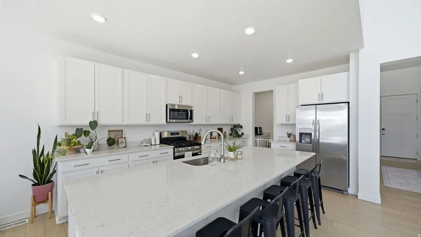 Contemporary kitchen featuring white cabinetry, stainless steel appliances, recessed lighting, a large island with seating, and light wood-finish flooring
