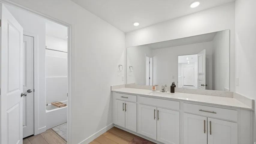 Double vanity with white shaker-style cabinetry, a light-toned countertop, and an expansive wall-mounted mirror