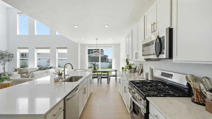 Spacious open-concept kitchen featuring light-finish cabinetry, stainless steel appliances, a gas range, and an expansive island with a built-in sink