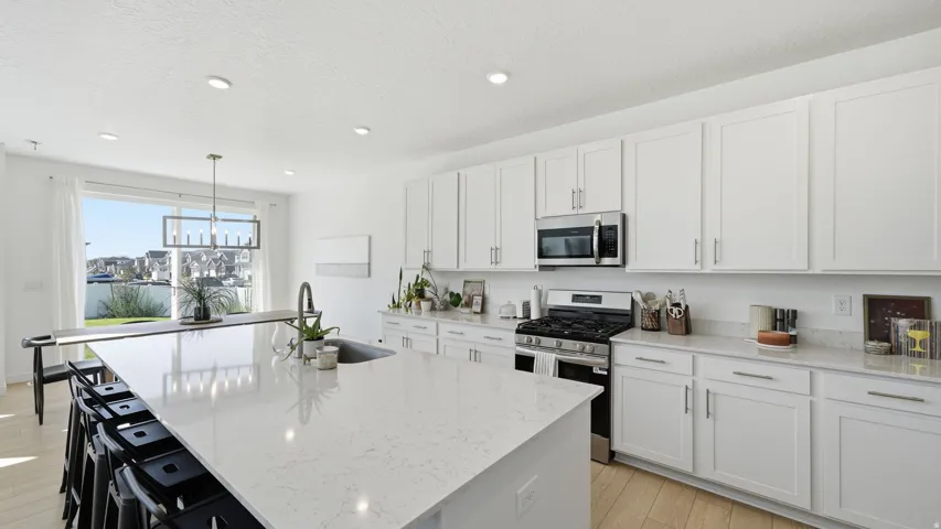 Sleek kitchen featuring white shaker cabinetry, stainless steel appliances, a large center island with a sink, and light wood-finish flooring