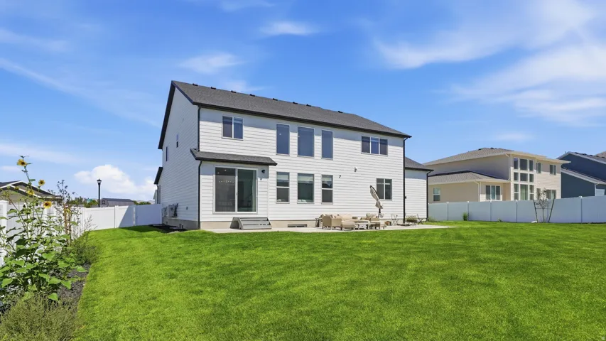 Expansive green lawn, white vinyl fencing, concrete patio, sliding glass door, and multiple windows across the rear facade