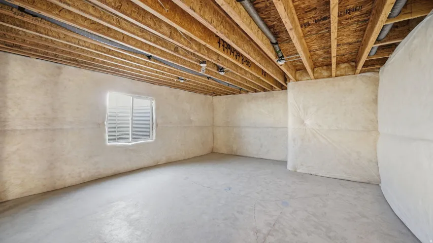Unfinished basement with exposed ceiling joists, concrete flooring, insulated walls, and a visible egress window
