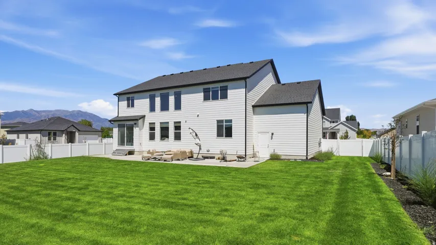 Expansive backyard featuring a manicured lawn, an extended patio, and a white privacy fence
