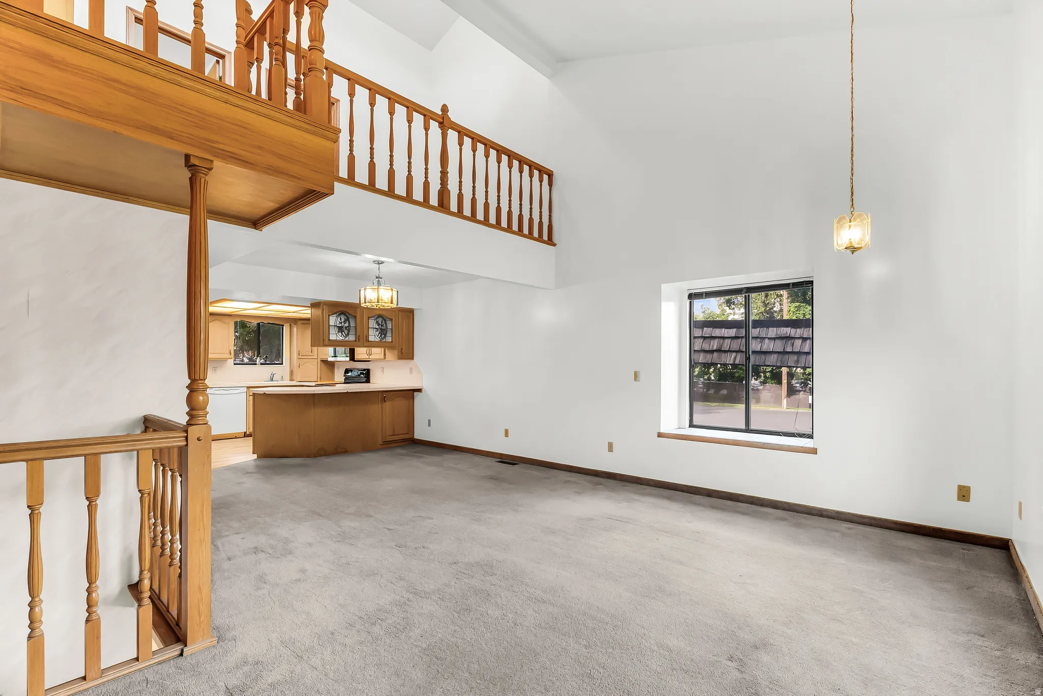 Vaulted ceilings, open loft, wood-finish railing, kitchen with wood cabinetry, and a large window