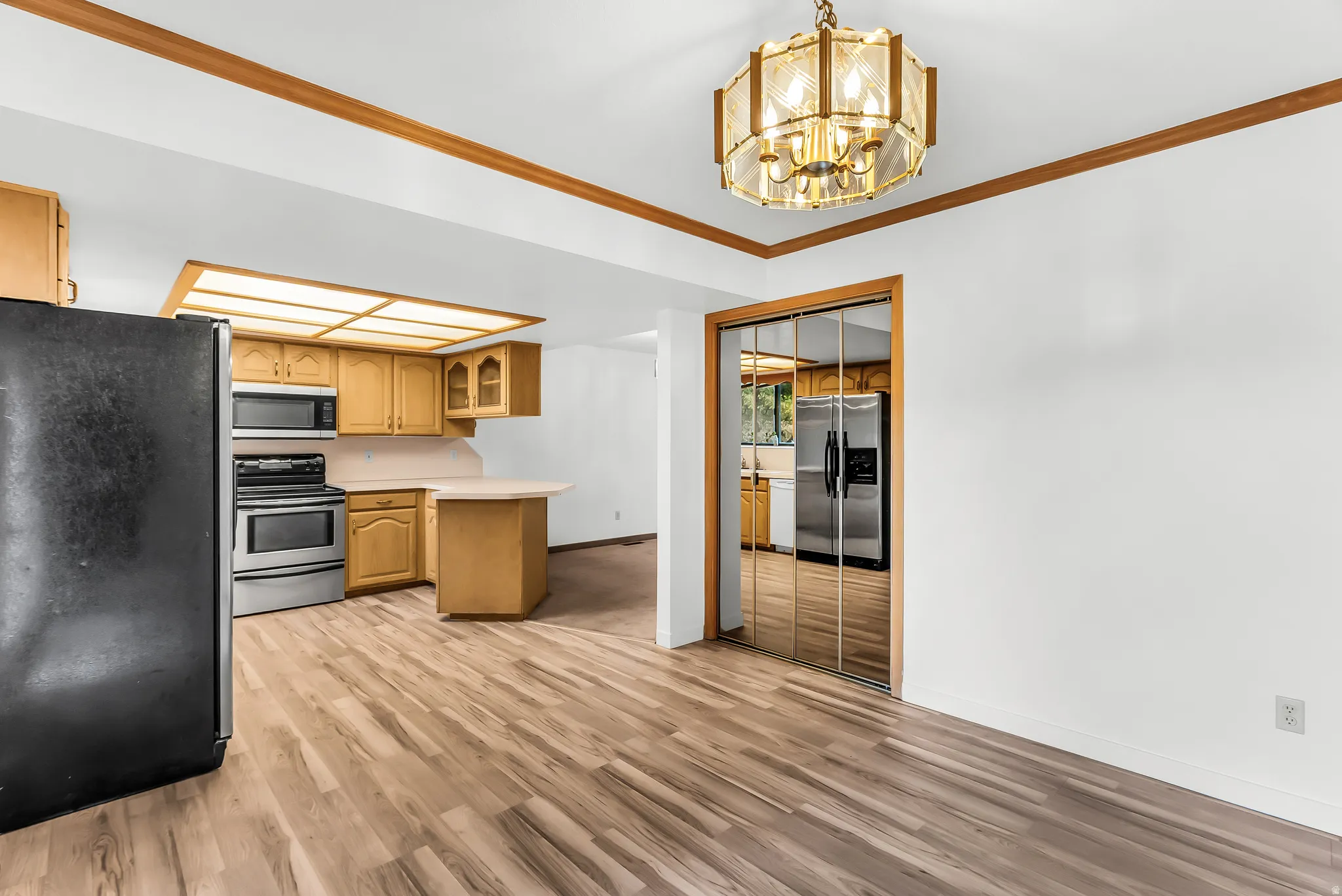 Wood-finish flooring, overhead lighting fixture, wood trim, kitchen cabinetry, and mirrored closet doors