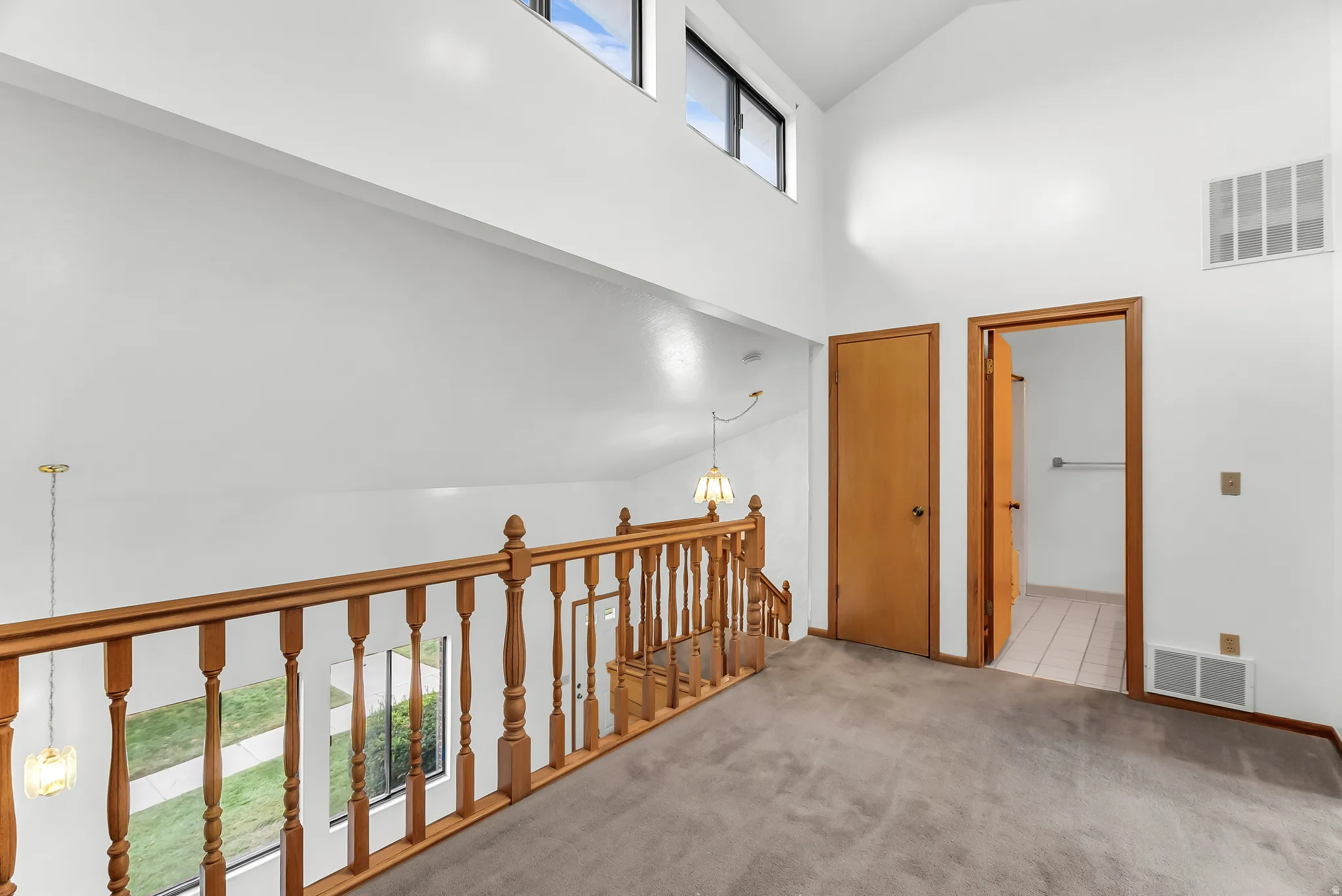 Vaulted ceiling, upper-level windows, wood spindle railing, and a tiled floor bathroom