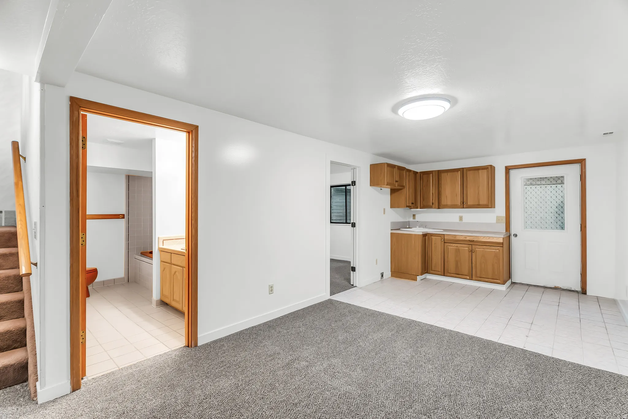Open-concept room featuring a functional kitchenette with wood cabinetry, a tiled floor section, and a separate carpeted area