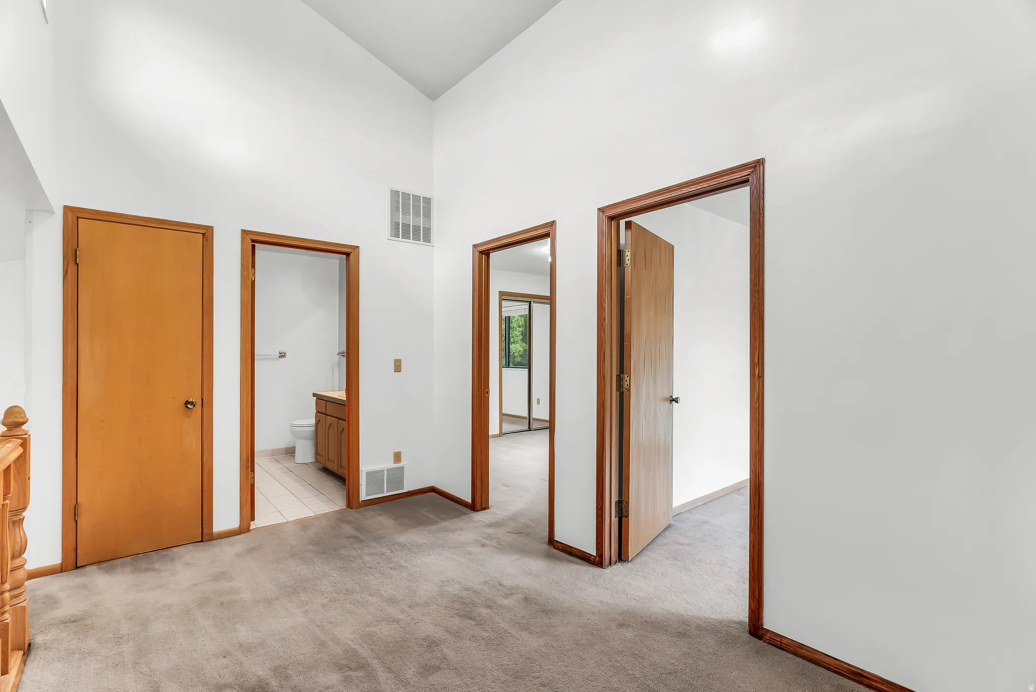Carpeted hallway with vaulted ceilings, featuring natural wood doors and trim