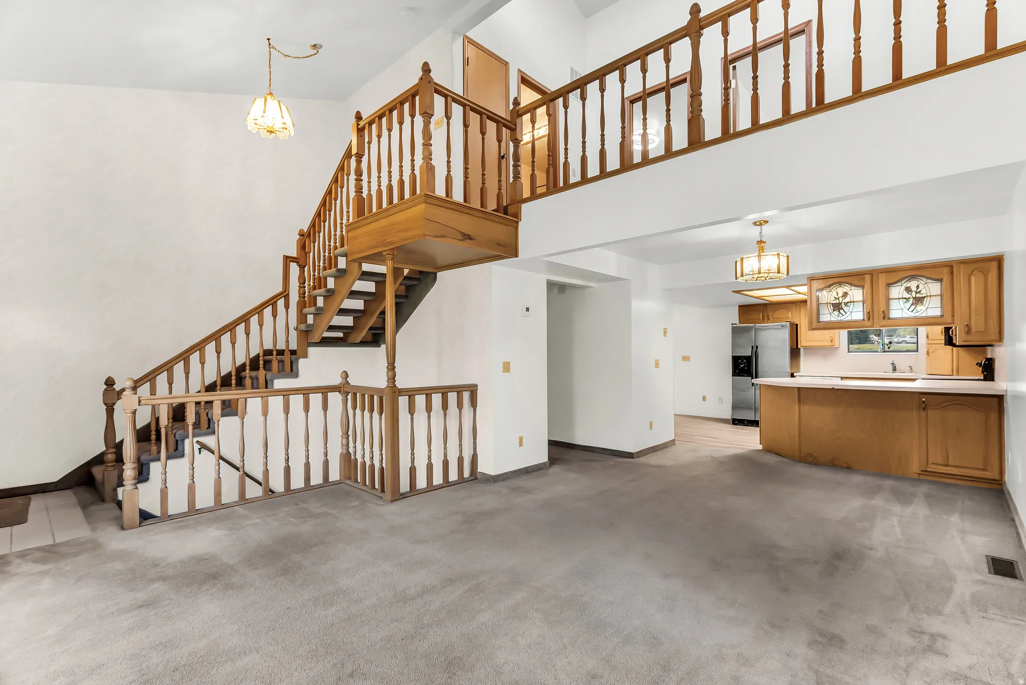 Two-story living area featuring a wooden staircase, light wood kitchen cabinetry, a kitchen island, and stainless steel appliances