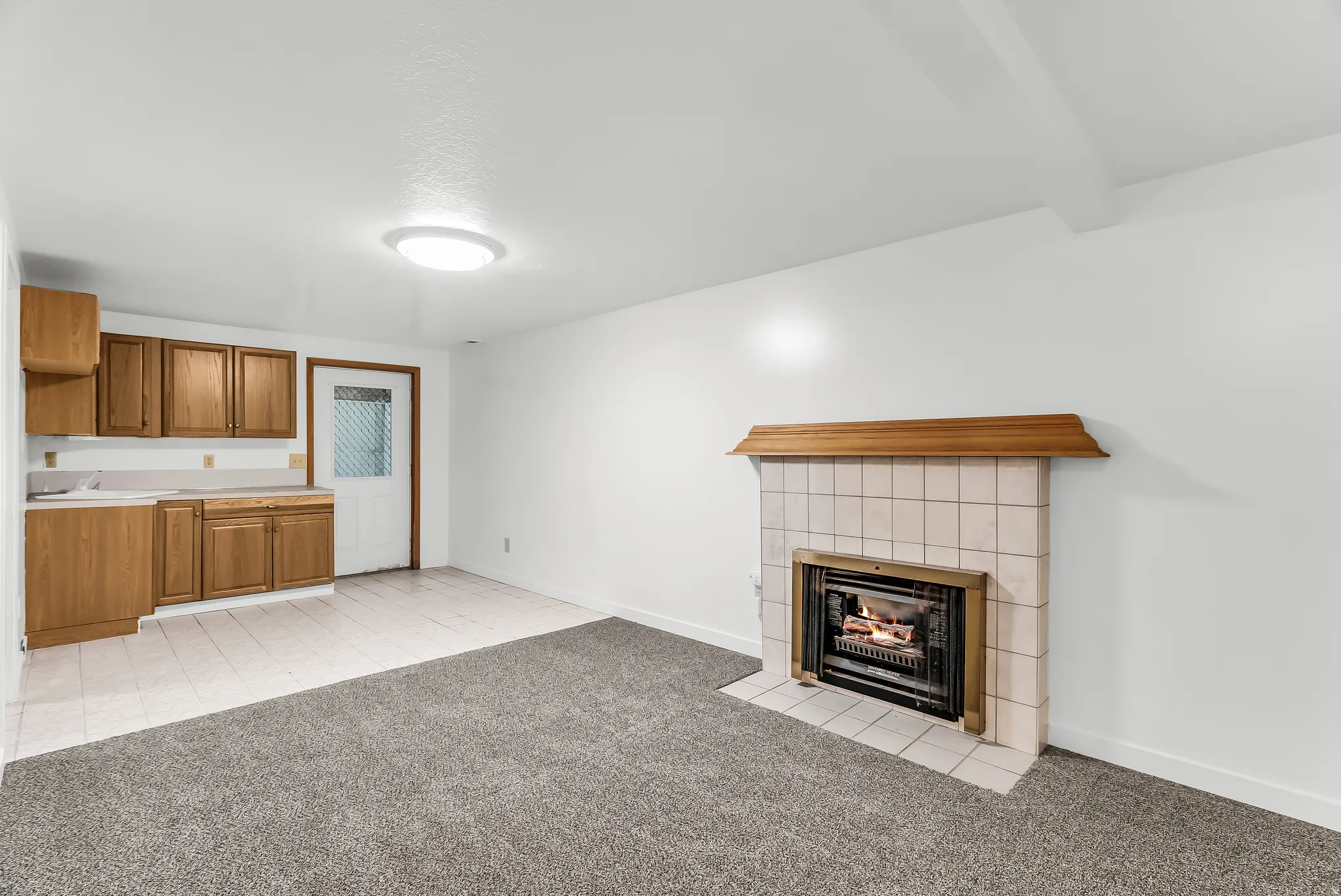 Living area featuring a fireplace with a tiled surround, a wood mantel, wood-finish cabinetry, and a combination of carpet and tiled flooring