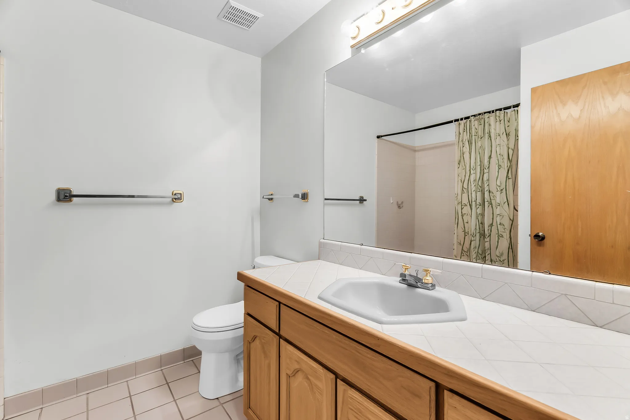 White tile flooring, wood-finish vanity with paneling, integrated sink, tiled countertop, and large wall-mounted mirror