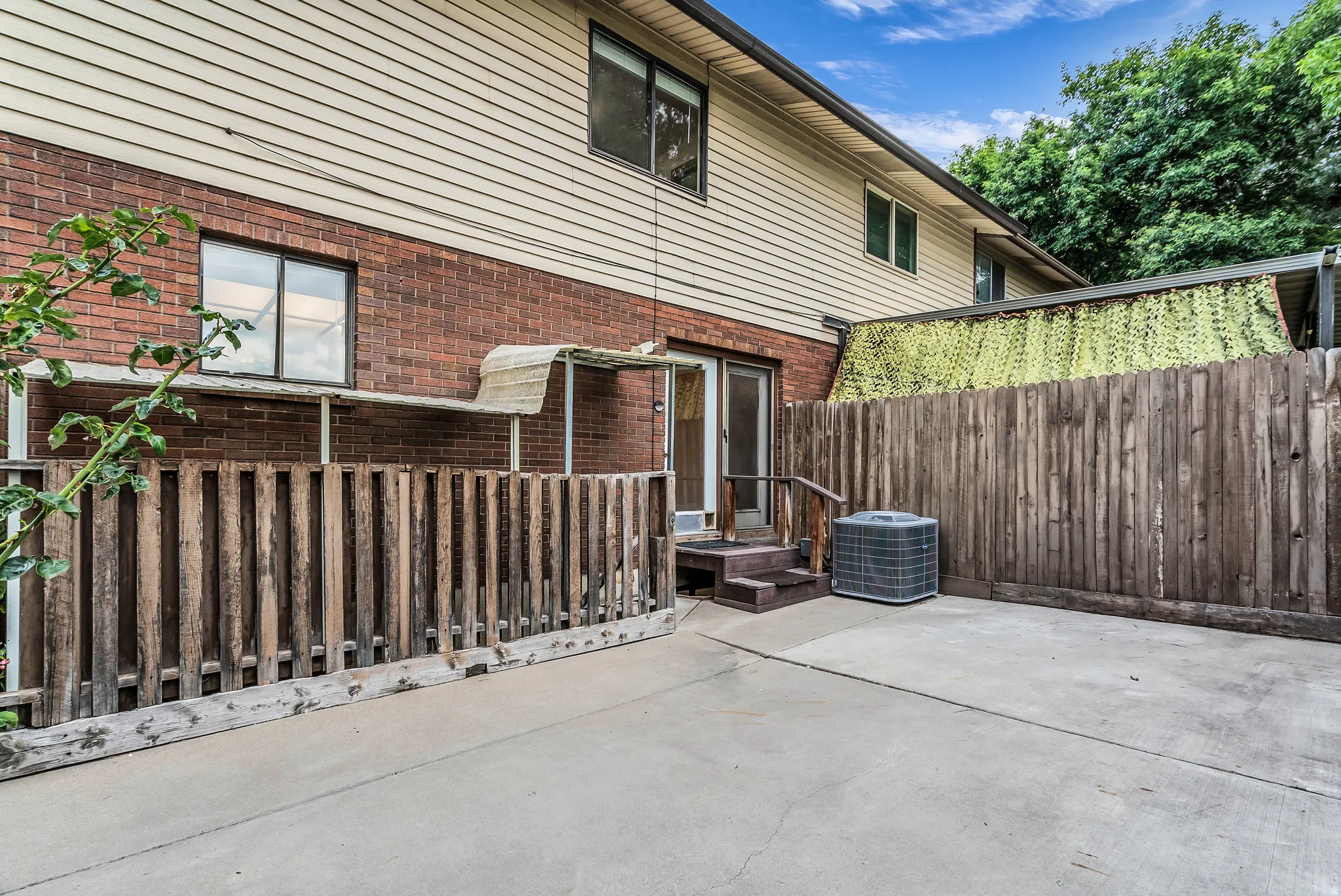 Concrete patio area with a wood privacy fence, brick exterior, and vinyl siding