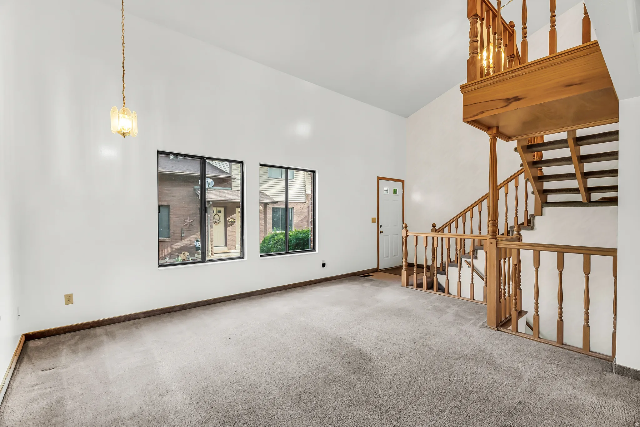Vaulted ceiling with a hanging fixture, natural wood staircase, and multiple windows