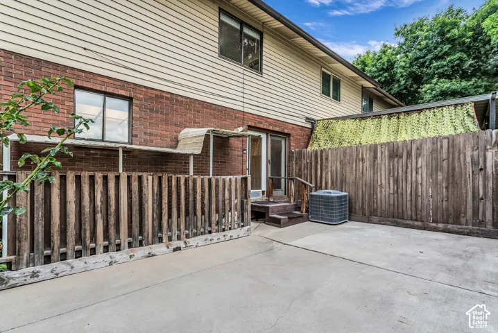 Concrete patio area with a wood privacy fence, brick exterior, and vinyl siding