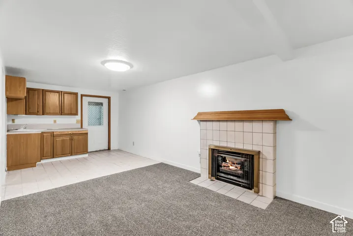 Living area featuring a fireplace with a tiled surround, a wood mantel, wood-finish cabinetry, and a combination of carpet and tiled flooring