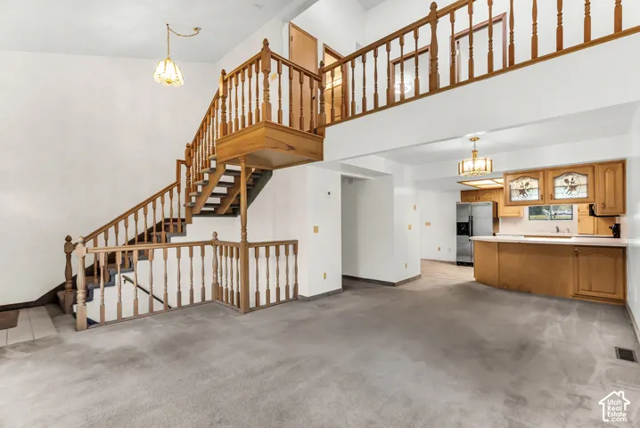 Two-story living area featuring a wooden staircase, light wood kitchen cabinetry, a kitchen island, and stainless steel appliances