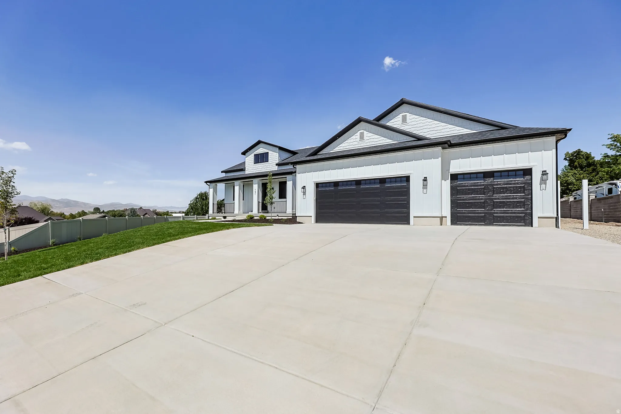 White exterior siding with dark trim accents, a multi-car garage with black doors, a covered porch with white columns, and a concrete driveway