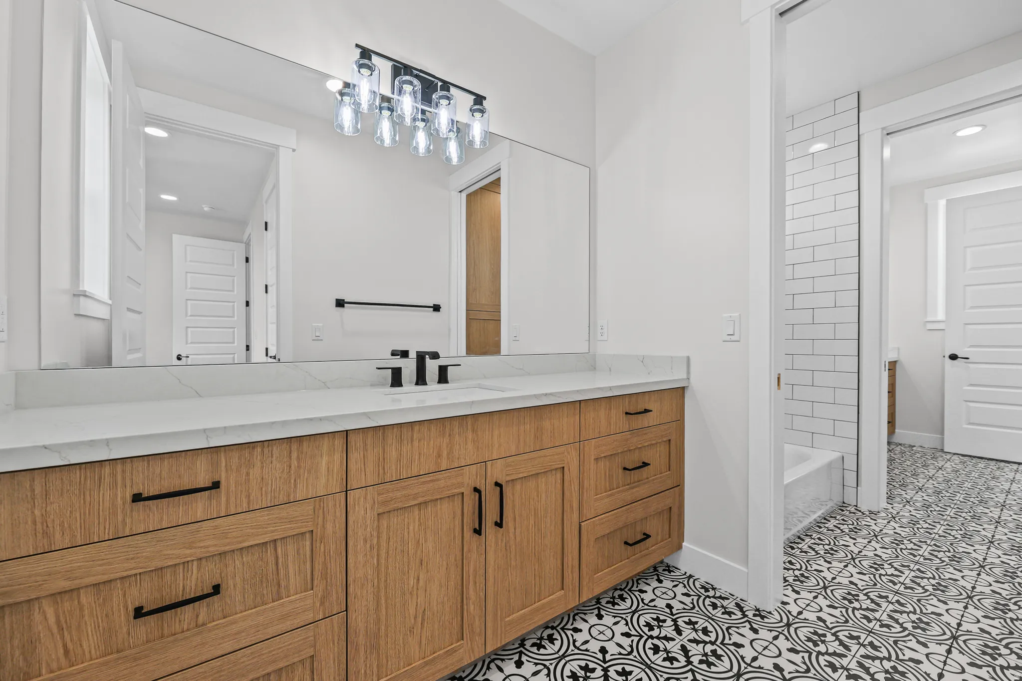 Wood-finish vanity with black hardware, white countertop, and patterned floor tile