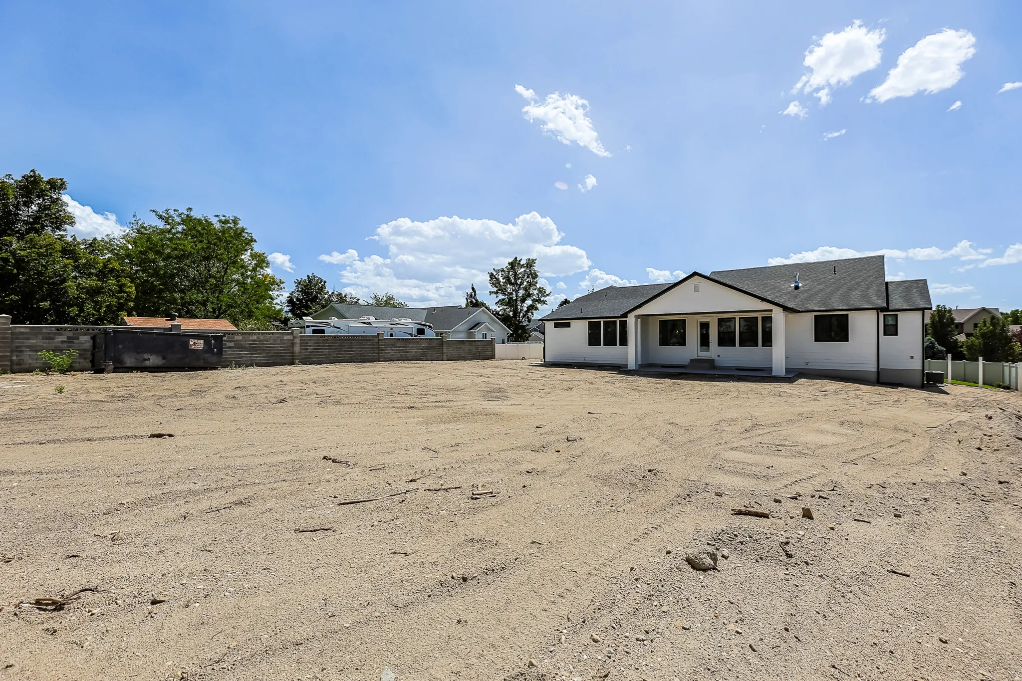 Expansive lot with a newly constructed residence featuring a covered patio, multiple windows, and a dark shingle roof