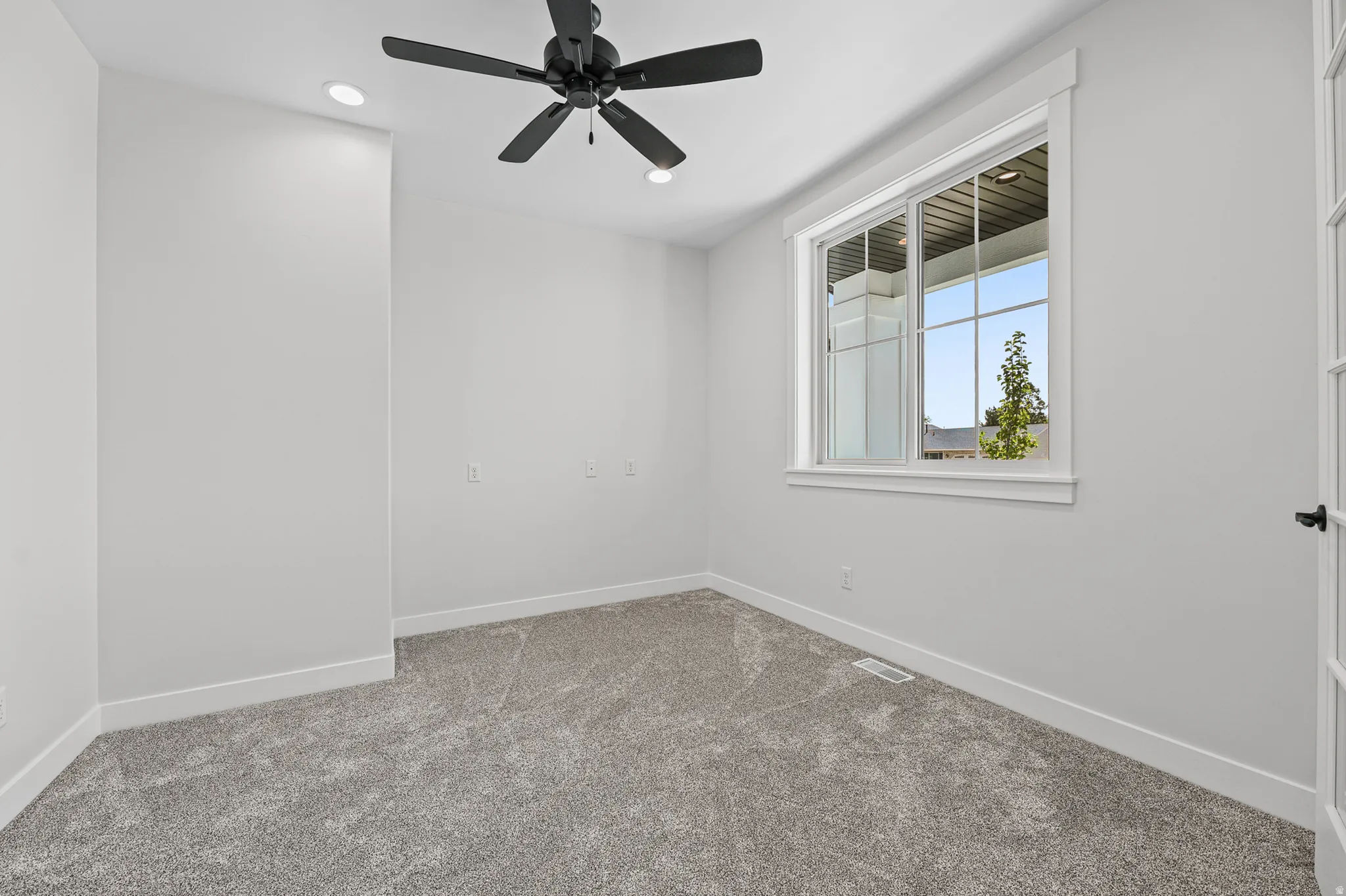 Recessed lighting, ceiling fan, grey carpeting, white trim, and a window with a multi-pane design