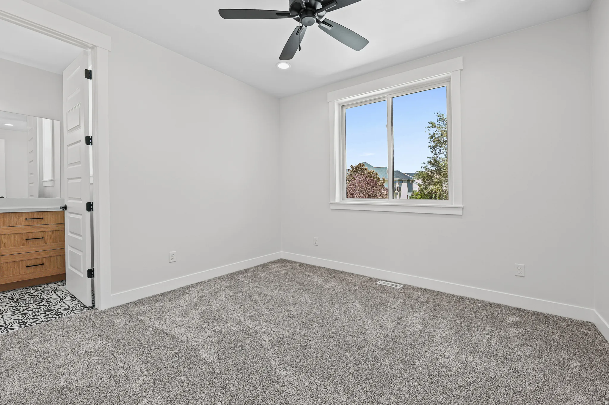 Plush gray carpeting with bright white walls, a black ceiling fan, and a large window with white trim