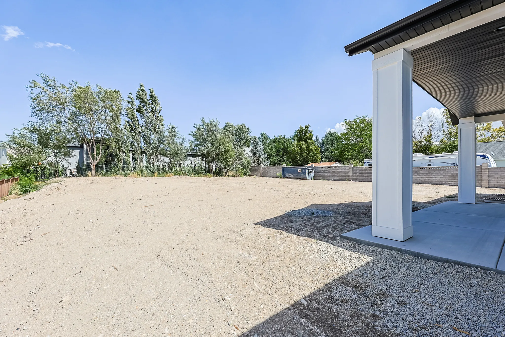 Expansive rear yard space with a covered patio area, solid concrete slab, and structural support columns