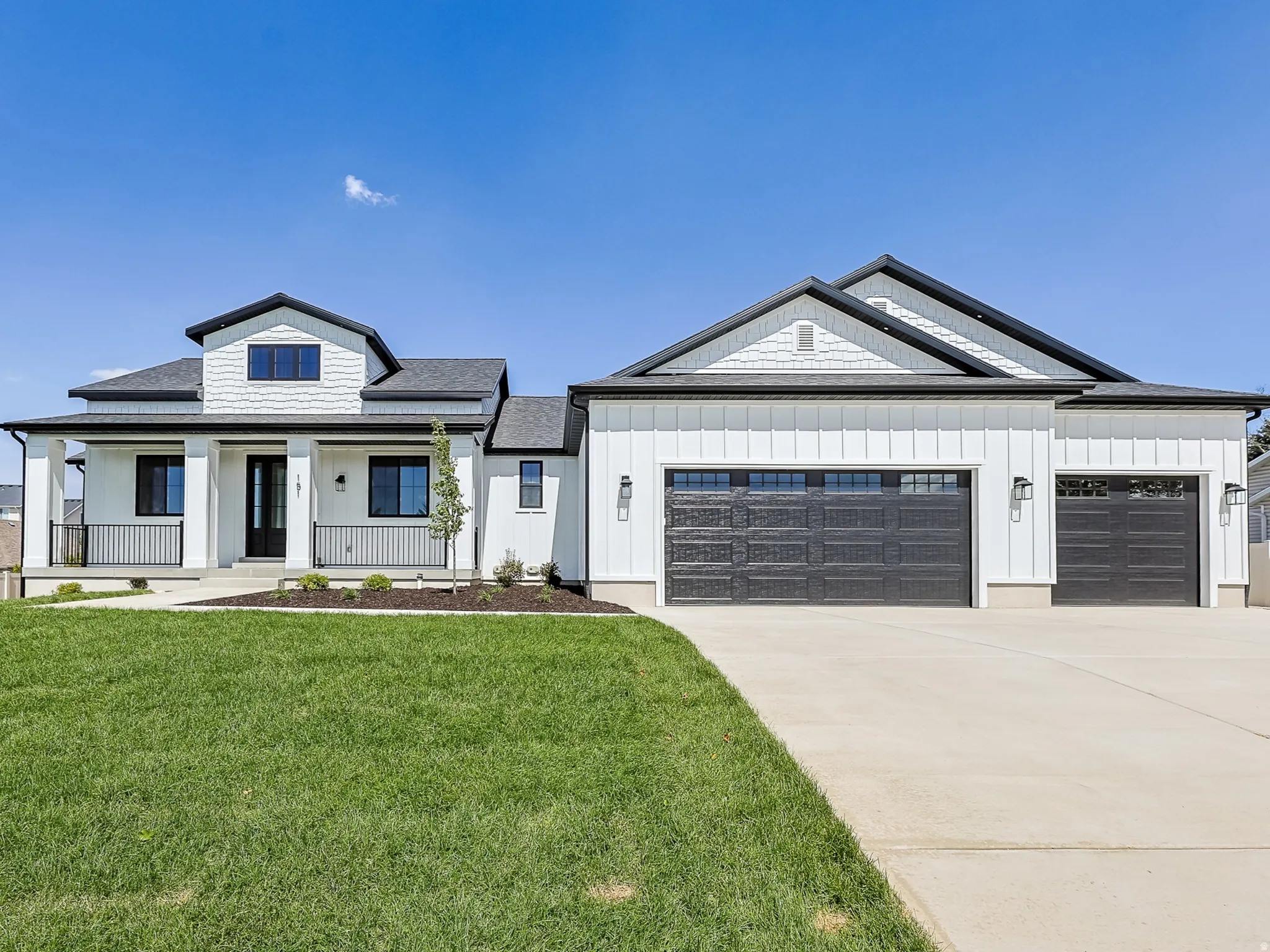 Modern farmhouse exterior with white vertical and horizontal siding, dark roof, and covered front porch with black railings