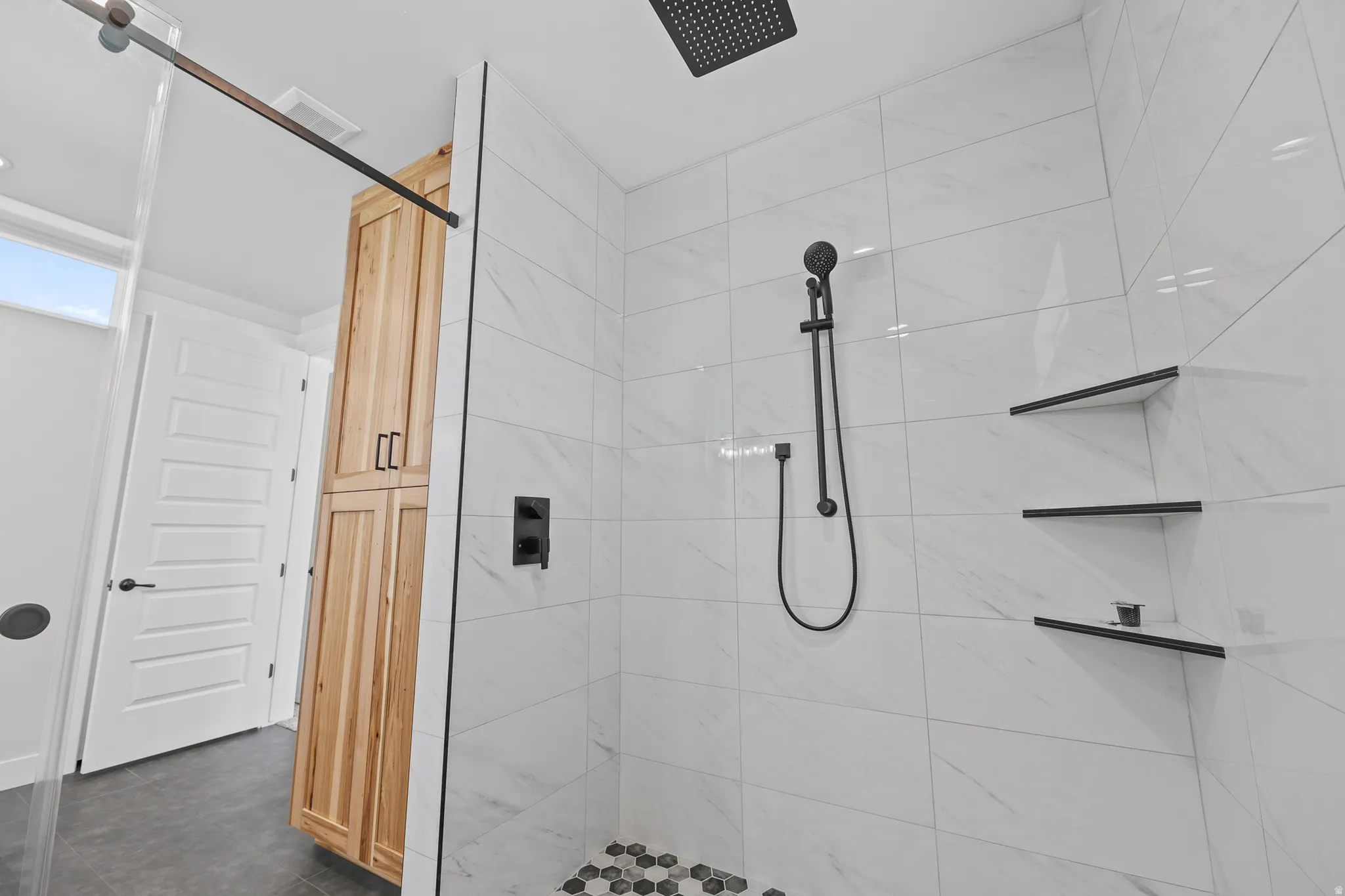Walk-in shower featuring a rainfall showerhead, handheld shower fixture, and built-in shelving