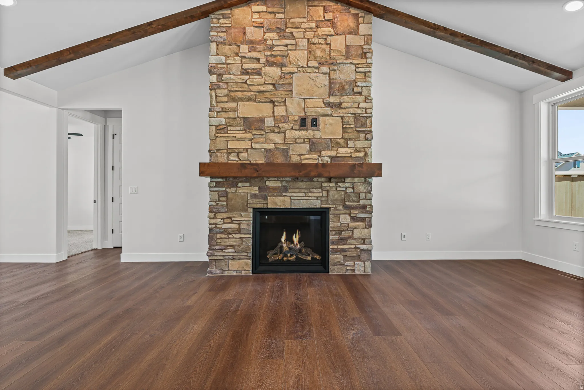 Stone-clad fireplace with a wood mantle, vaulted ceilings, exposed ceiling beams, and wood-finish flooring