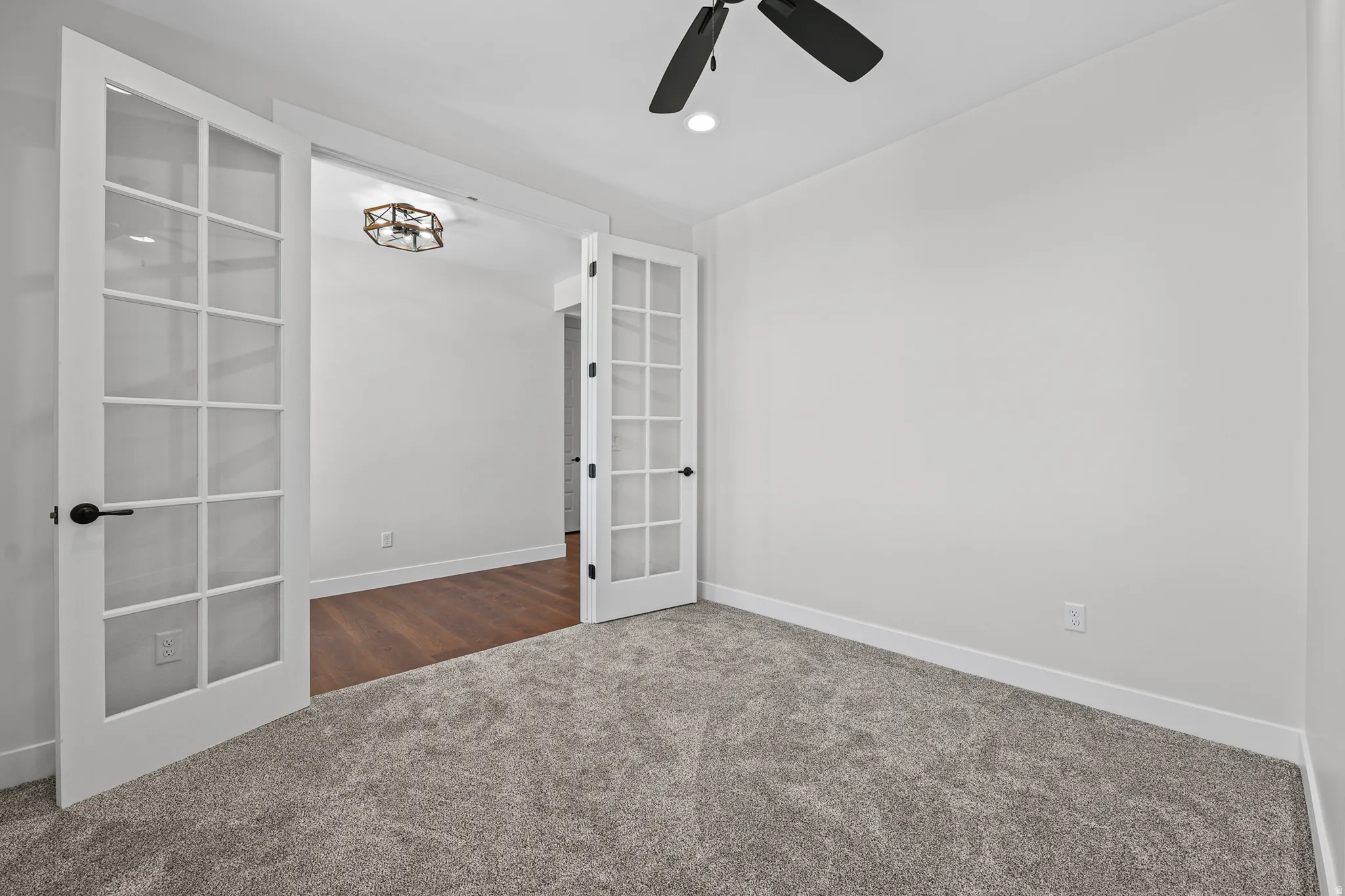 French doors with divided lites, ceiling fan with light fixture, recessed ceiling lighting, light gray carpeting, and wood-finish flooring visible beyond the doorway