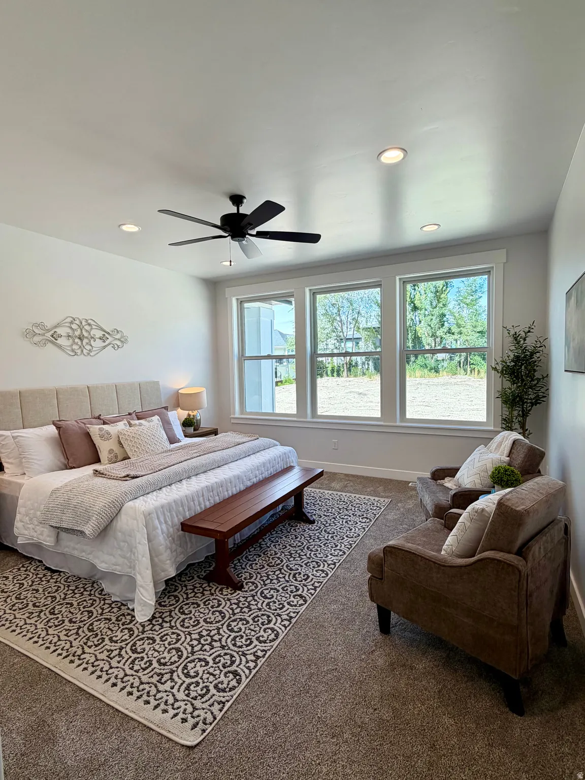 Recessed ceiling lighting, ceiling fan, multiple large windows, wall-to-wall carpeting, and an upholstered headboard