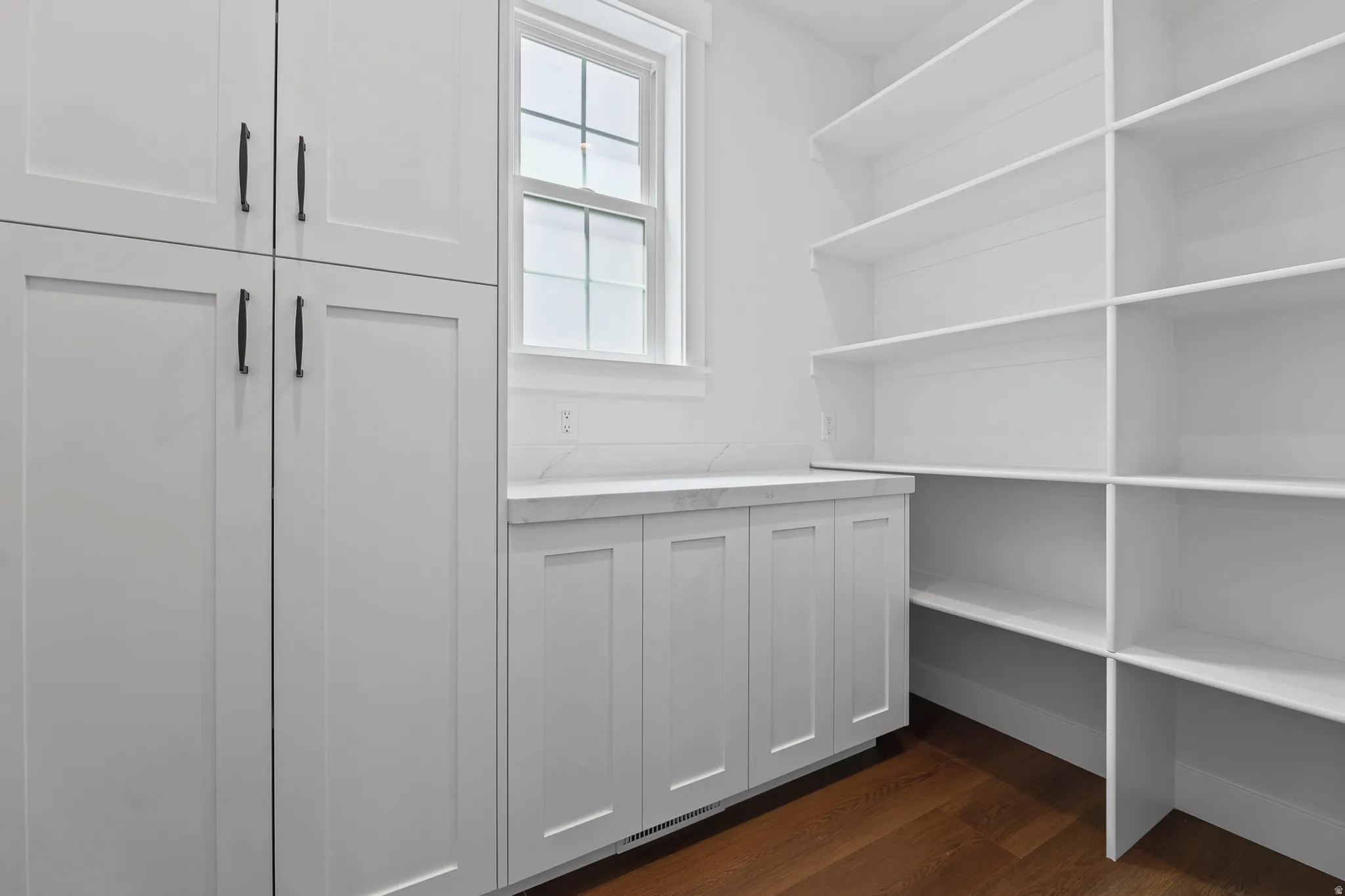 Built-in cabinetry with dark hardware, white countertop, white subway tile backsplash, window, and wood-finish flooring