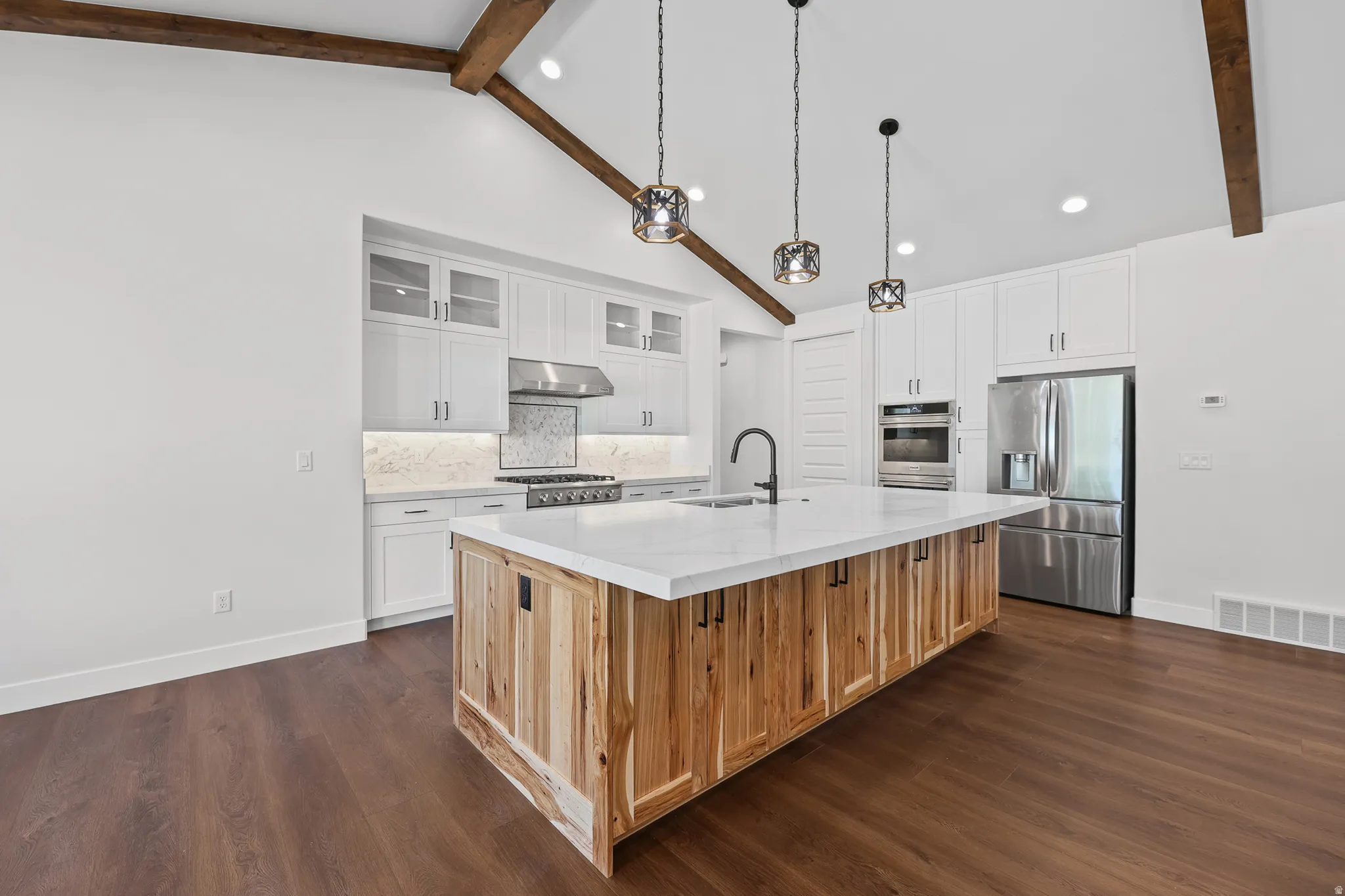 Kitchen with vaulted ceilings, exposed wood beams, wood-finish flooring, a large island with a light-toned countertop, and stainless steel appliances