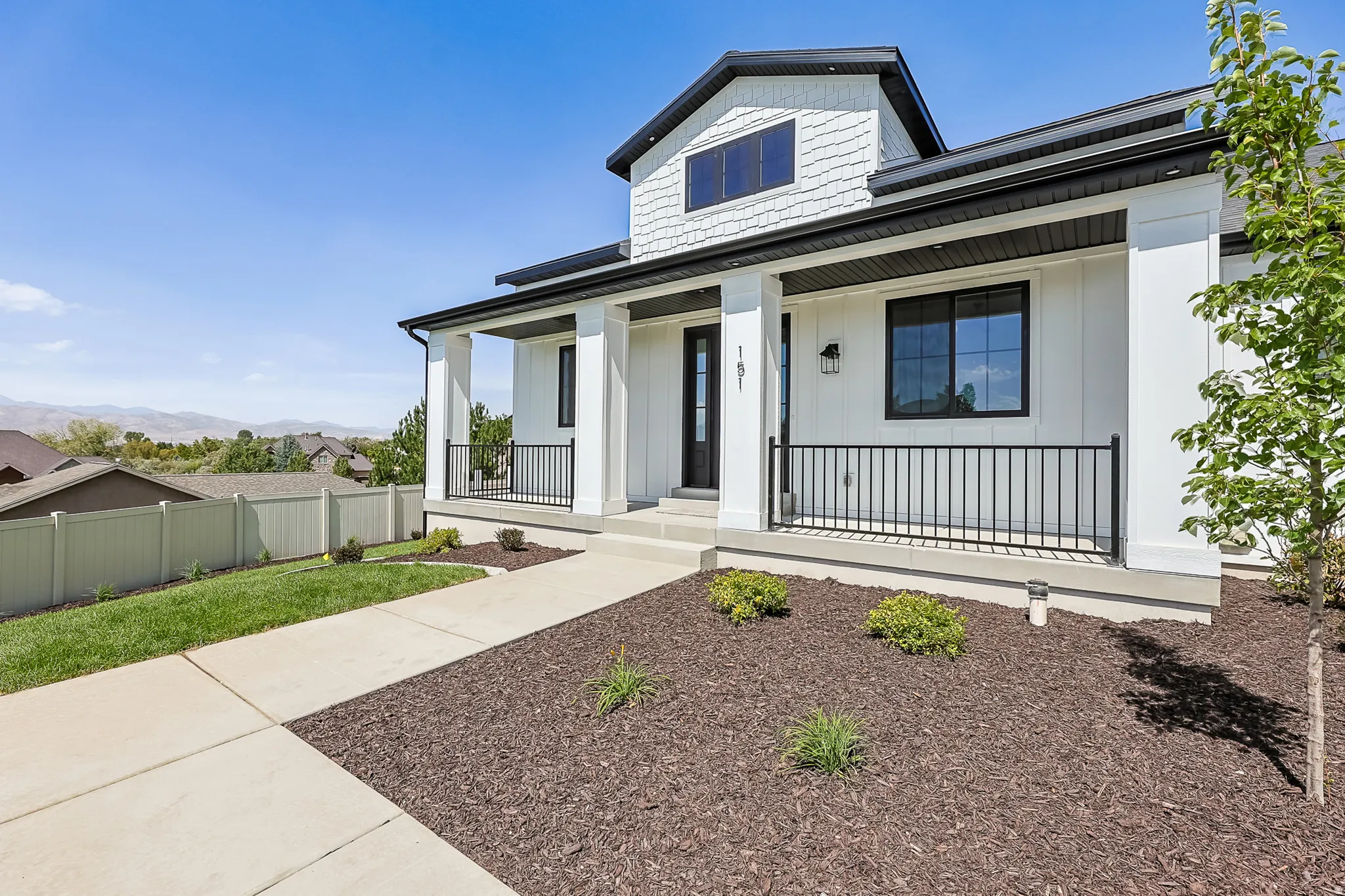 Contemporary two-story exterior featuring white siding, black-framed windows, a covered front porch with black railings, and a dormer window
