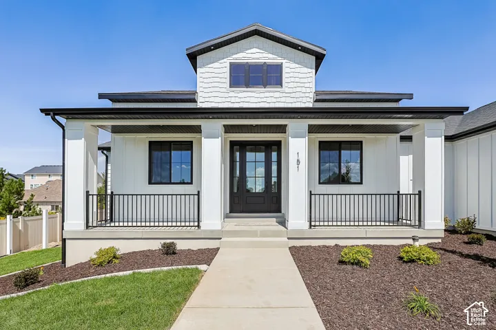 Covered front porch with square columns, black metal railings, a dark paneled entry door, and dark window frames