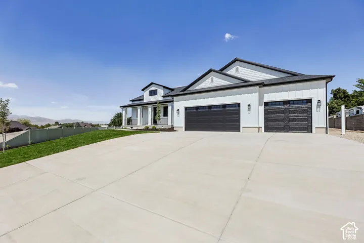 White exterior siding with dark trim accents, a multi-car garage with black doors, a covered porch with white columns, and a concrete driveway